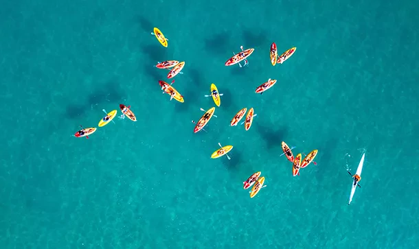 Vue aérienne de kayaks colorés sur l'eau, symbolisant la coordination et l'organisation logistique pour la location de salles à la CVCI.